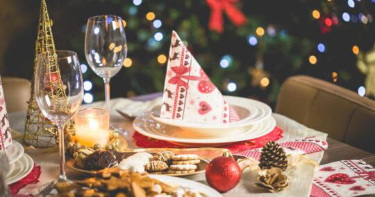 A decorated holiday dinner table set with Christmas tree and bokeh lights in the background