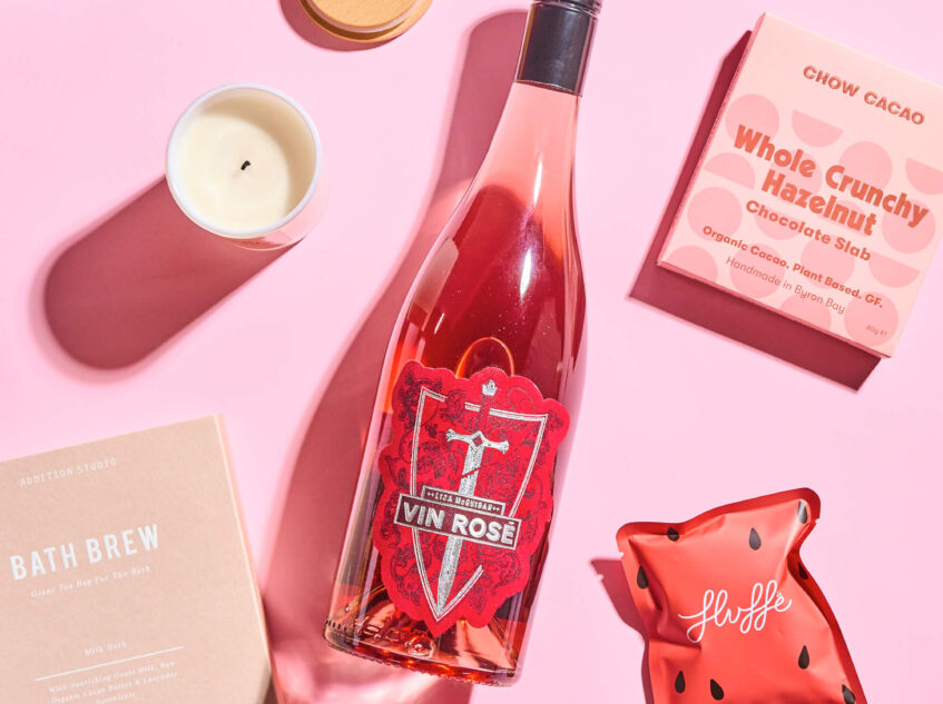Gift set with a bottle of rosé wine, chocolate bar, bath brew, candle, and other self-care items in a pink box with 'Somebody Loves You' written on it