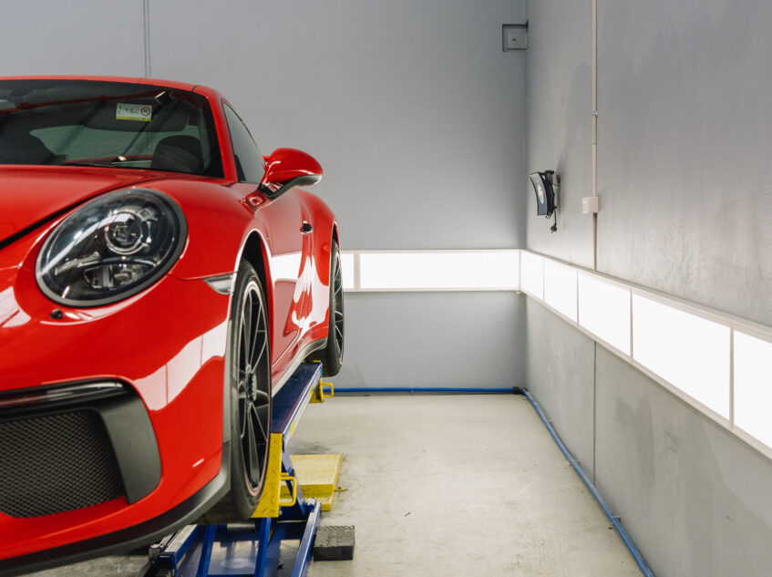 Side view of a red luxury car elevated on a lift in a modern automotive service area